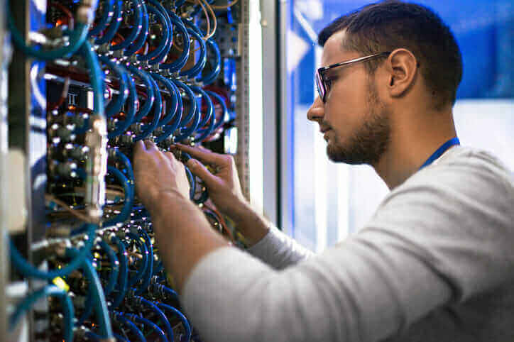 Technician performing breakfix maintenance on server rack with cables in data center.