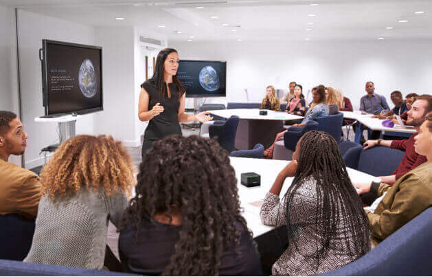 Modern meeting room with diverse team using Crestron Flex Pods, interactive displays, and collaborative seating arrangement.